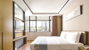 Une chambre d’hôtel moderne dotée d’un grand lit, d’une table de chevet, d’un téléviseur intégré et offrant une vue sur les palmiers et les immeubles grâce à de grandes fenêtres.