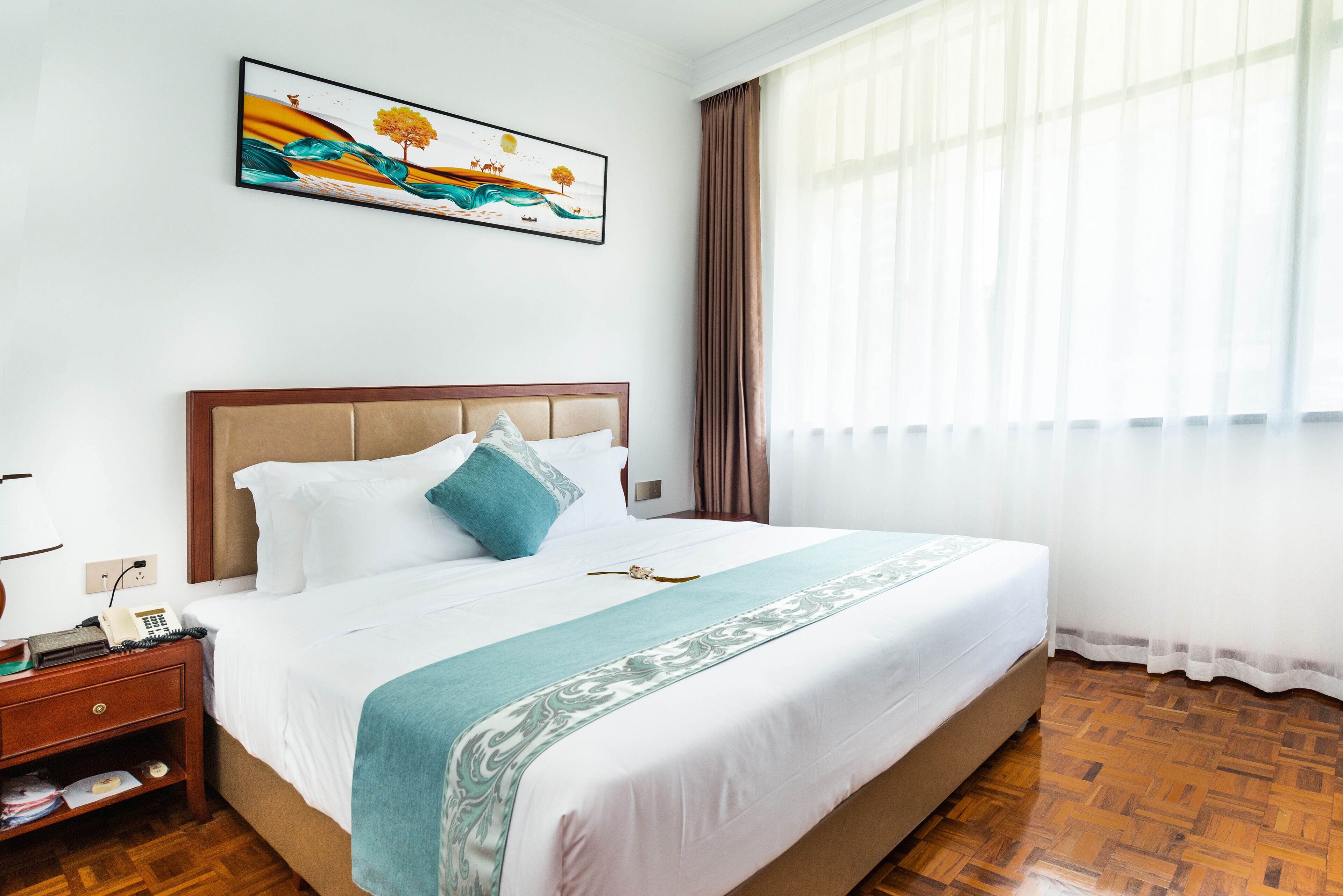 Una cama bien hecha con una colcha estampada, una mesita de noche con una lámpara y un cuadro en la pared.