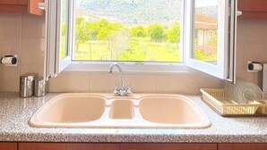 Une cuisine équipée d’un évier à deux bacs, de meubles en bois et d’une fenêtre donnant sur un paysage verdoyant et vallonné.