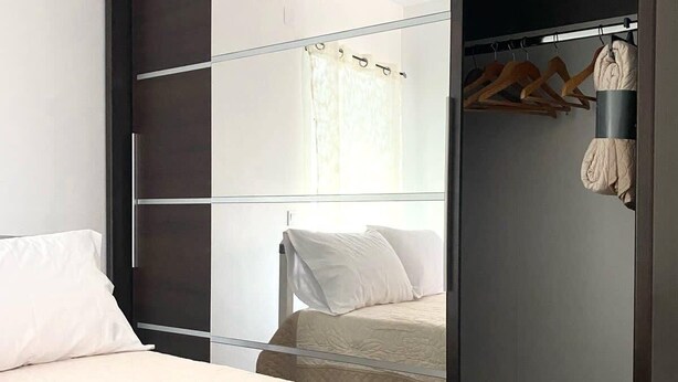 Une chambre moderne avec un grand lit, une armoire à portes coulissantes et un portant à vêtements.