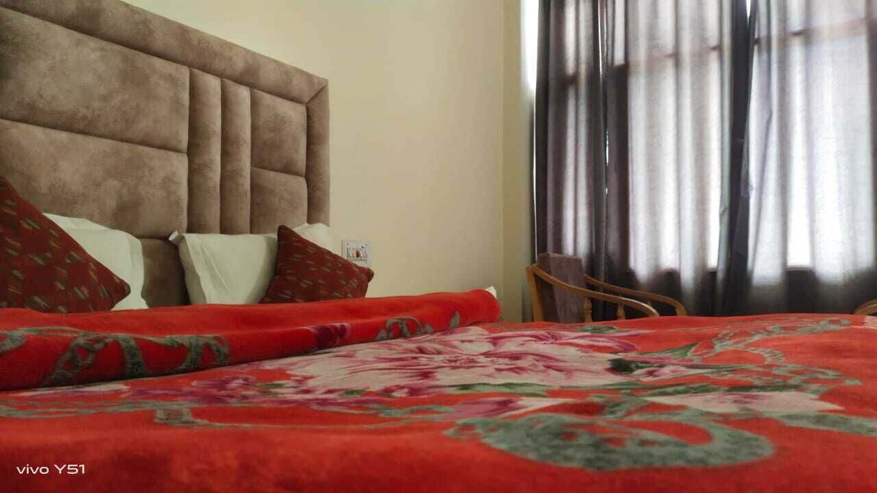 Une chambre d’hôtel avec un grand lit, une tête de lit, une chaise et une fenêtre avec des rideaux.