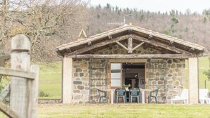Un bâtiment en pierre avec un toit à deux versants, un petit porche avec deux chaises et une table.