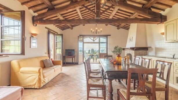 Un vaste espace dédié à la salle à manger, avec une table et des chaises en bois, un canapé et une vue sur l’extérieur grâce à de grandes fenêtres.