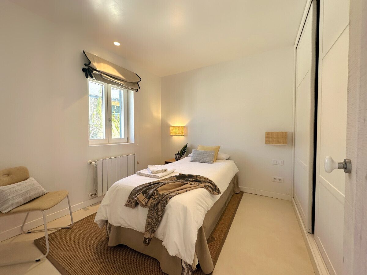Une chambre à coucher comprenant un lit, une chaise, un radiateur, une fenêtre avec des rideaux et un luminaire fixé au mur.