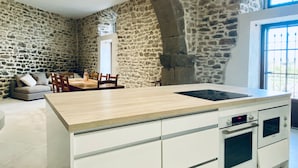 A kitchen with a stone wall, a wooden dining table, and a built-in oven. - Step into French history at Le Bastion, Pouzols-Minervois, southern France. (Pouzols-Minervois)