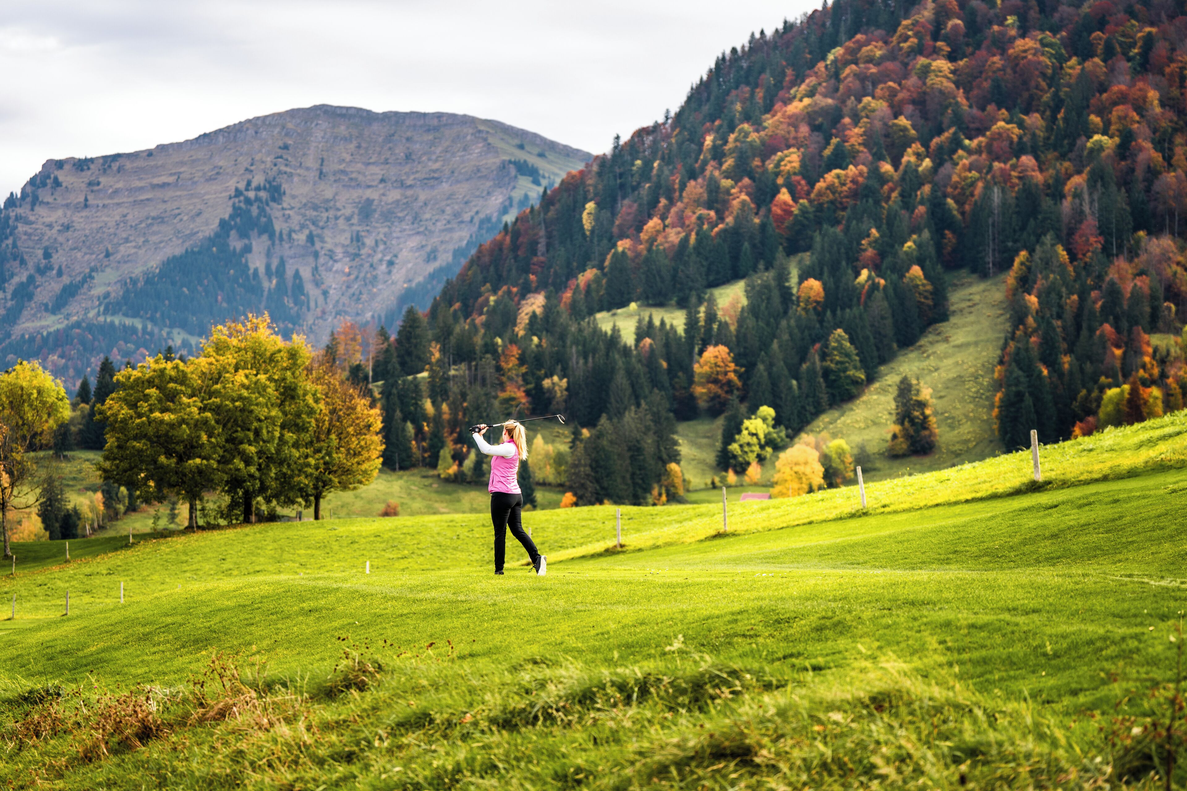 A golf course with a hilly backdrop and a single golfer in motion.