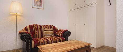 A room with a sofa, a wooden table, a floor lamp, and a wardrobe.