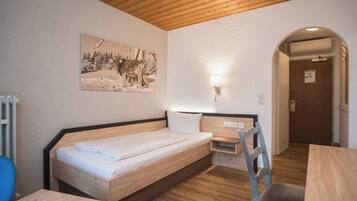 Una habitación con una cama de madera, un escritorio, una silla, una lámpara de pared y una puerta.