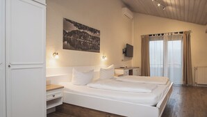 Ein Schlafzimmer mit einem großen Bett, Nachttischen, einem an der Wand montierten Fernseher und einem Fenster mit Vorhängen.