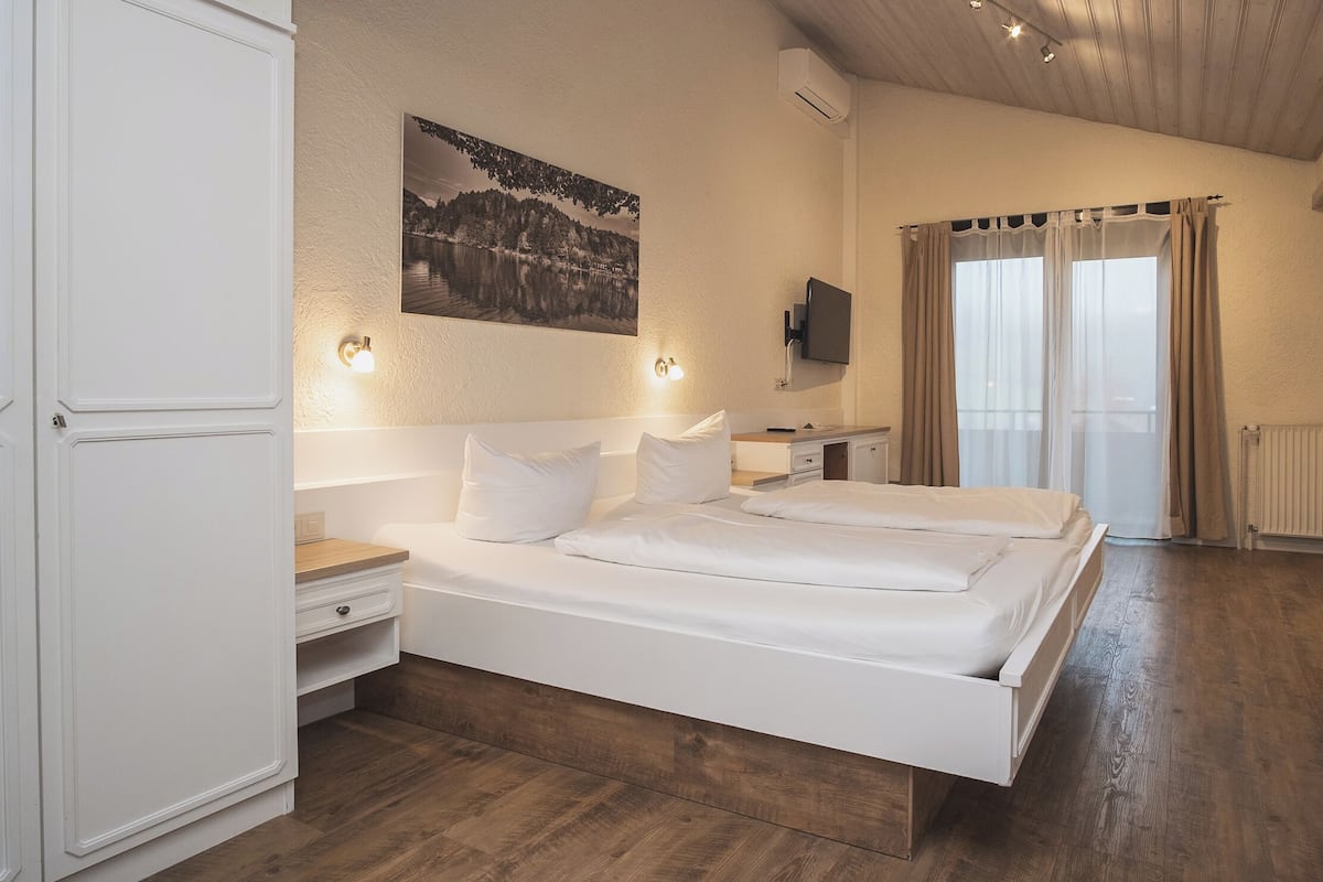 A bedroom with a large bed, bedside tables, a mounted TV, and a window with curtains.