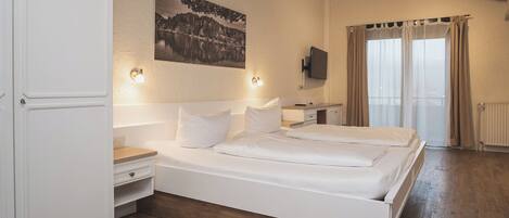 Een slaapkamer met een groot bed, nachtkastjes, een wandtelevisie en een raam met gordijnen.