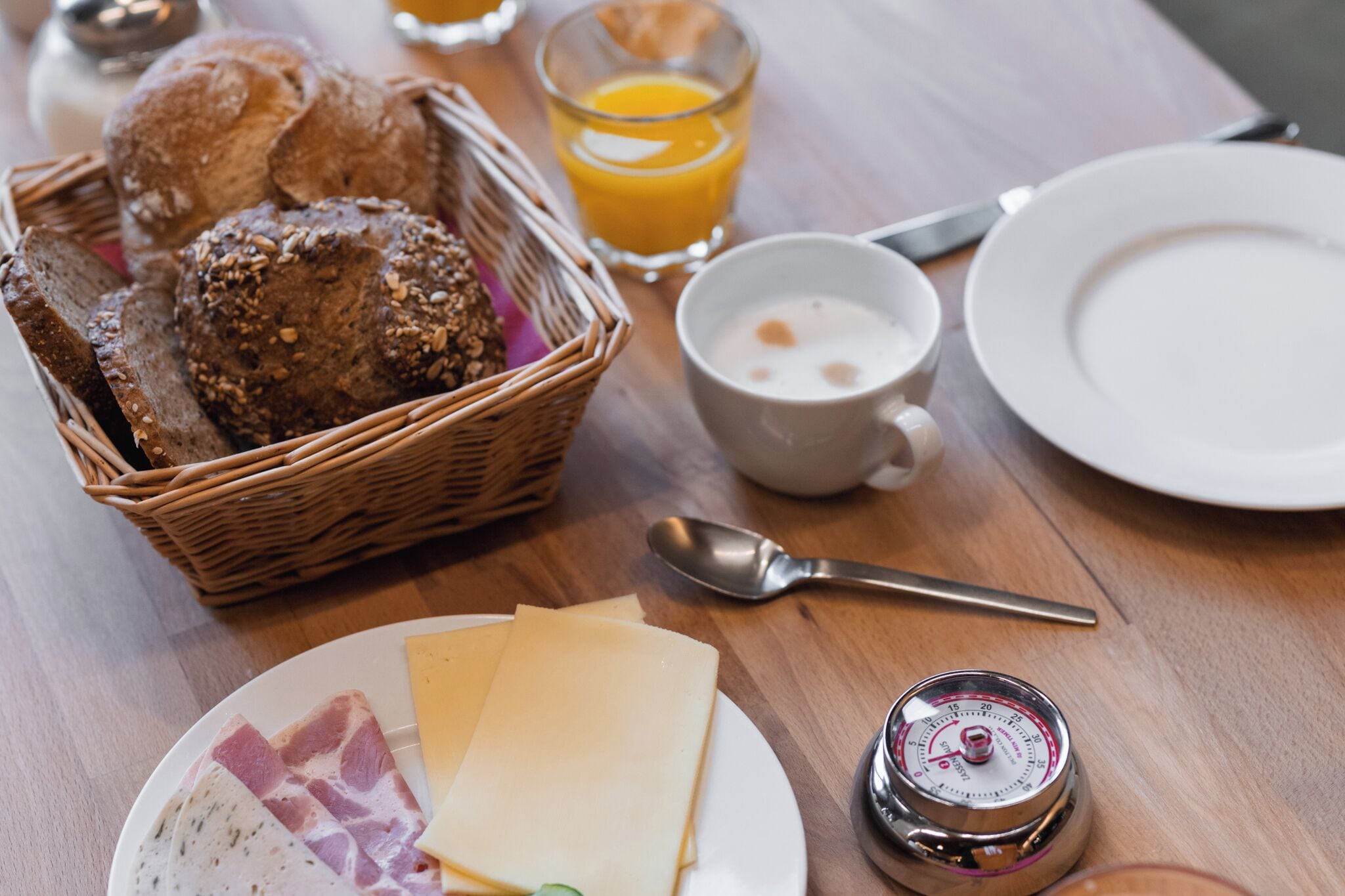 A breakfast setting with bread, cheese, ham, a cup of coffee, a glass of orange juice, and a thermos.