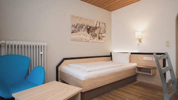 Une chambre avec un lit en bois, une chaise bleue, une petite table, une lampe fixée au mur et un tableau représentant une vache.