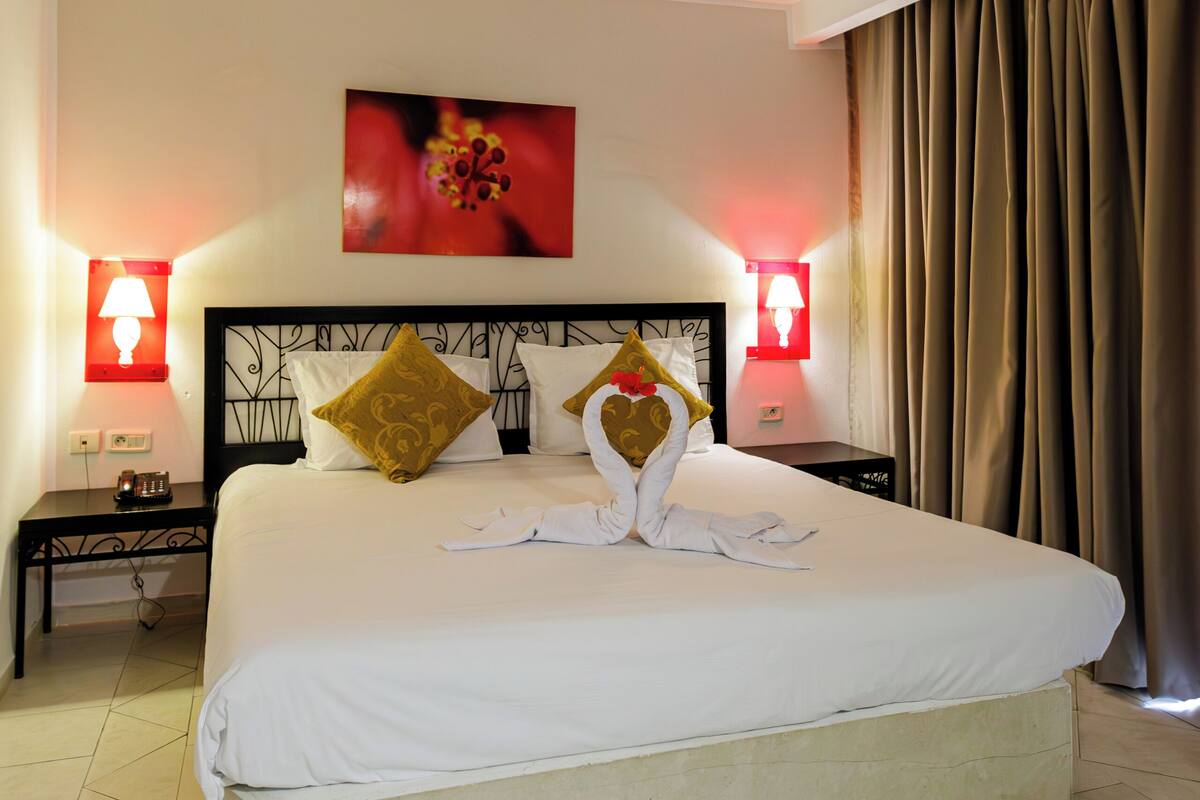 A hotel room with a large bed, two bedside lamps, a headboard, and a painting on the wall.