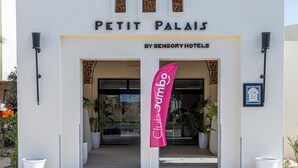 A hotel entrance with a sign reading "PETIT PALAIS BY SENSORY HOTELS" and a pink flag with "Club" on it. - Le Petit Palais Djerba & Spa (Djerba Midun)