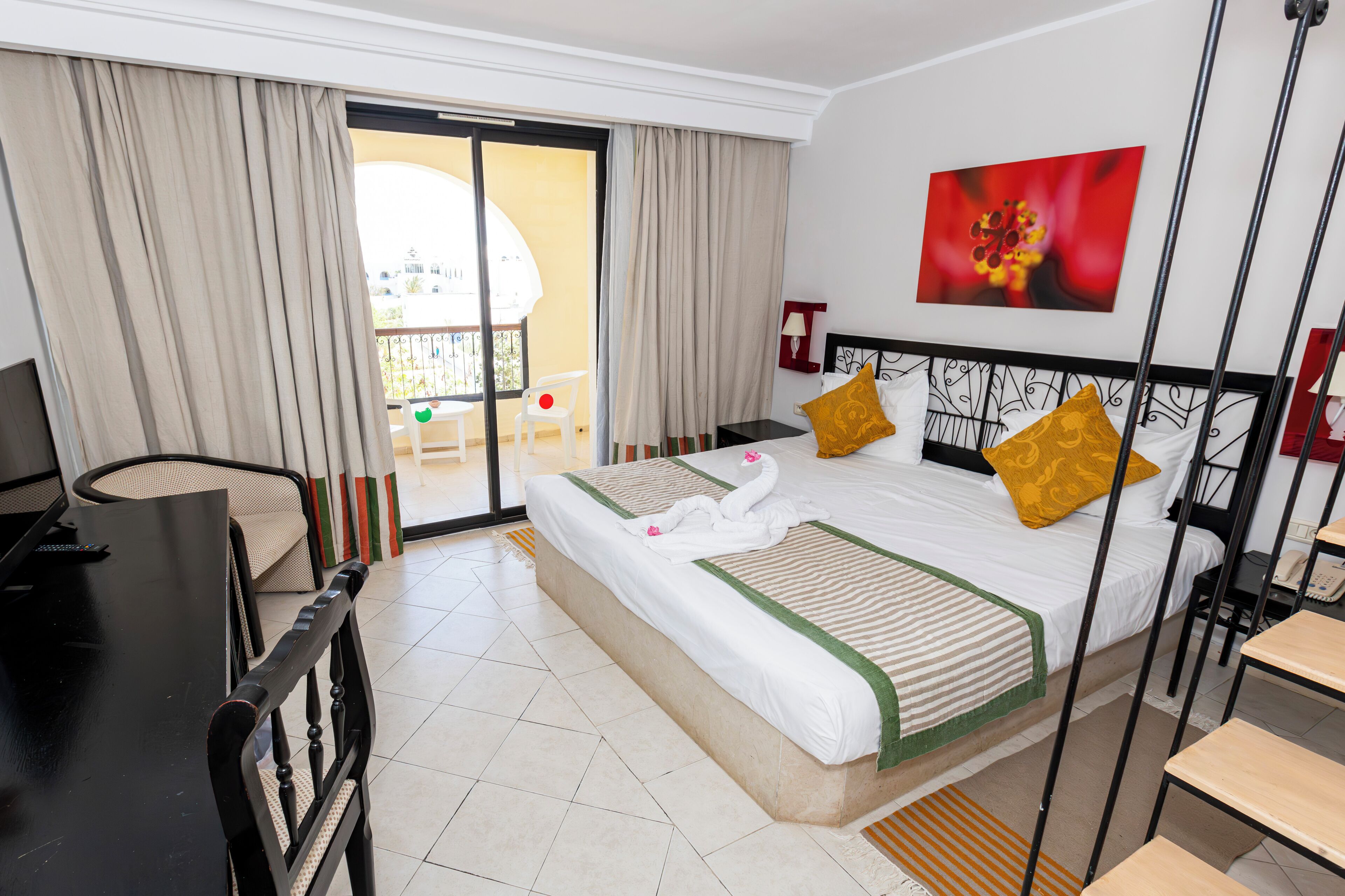 A hotel room with a bed, a desk, a chair, and a balcony with a table and chairs.