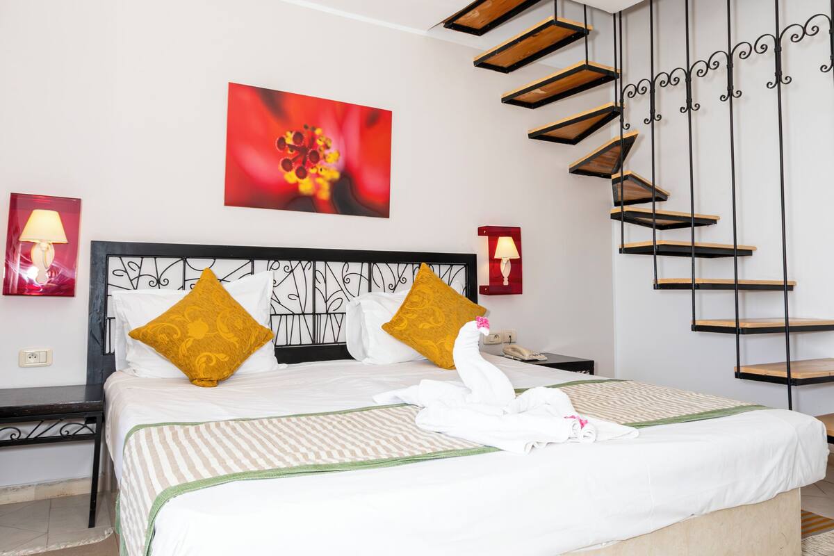 A hotel room with a bed, a staircase, and a red flower painting on the wall.