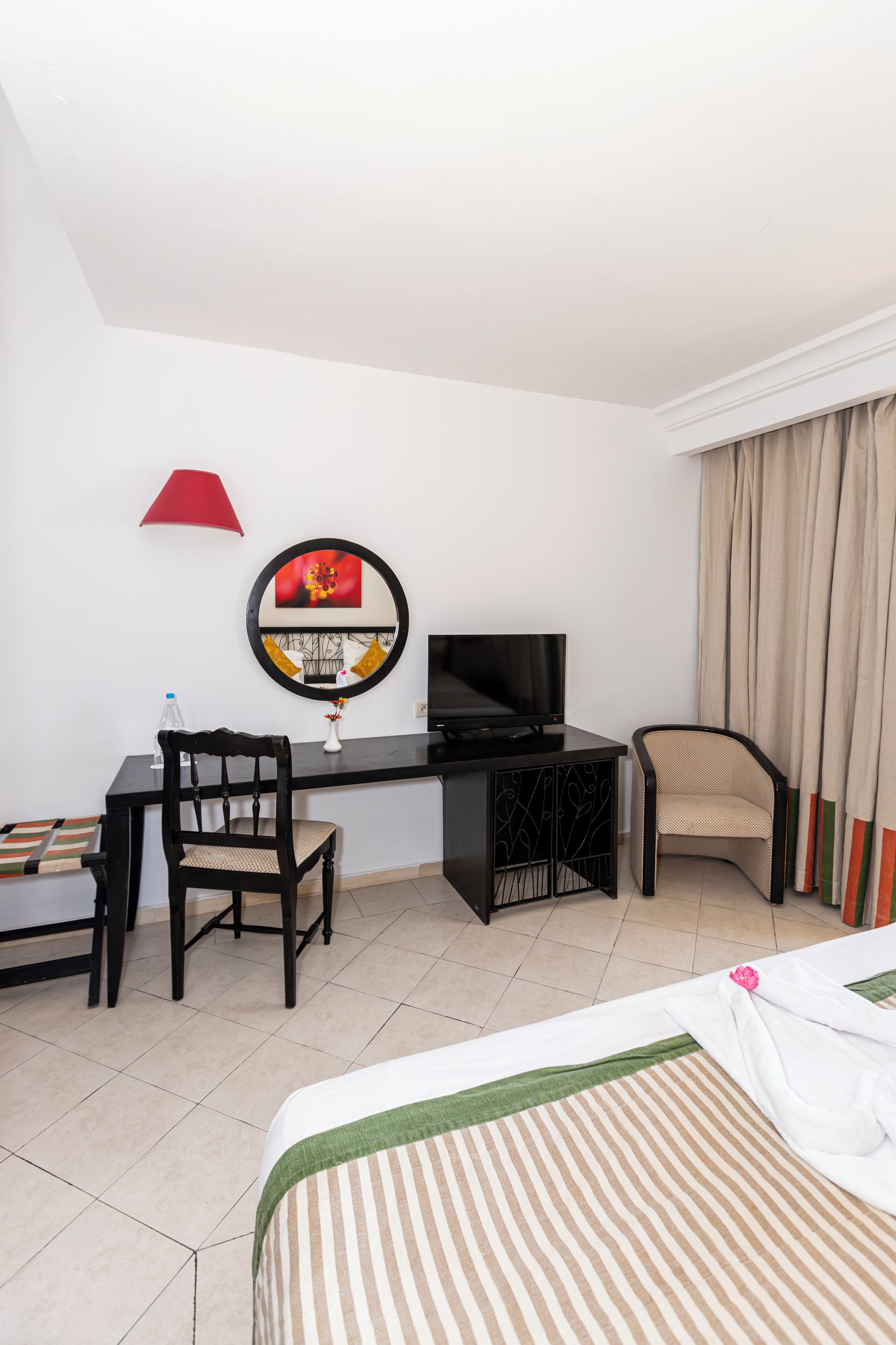 Een hotelkamer met een bed, een bureau met stoel, een televisie en een raam met gordijnen.