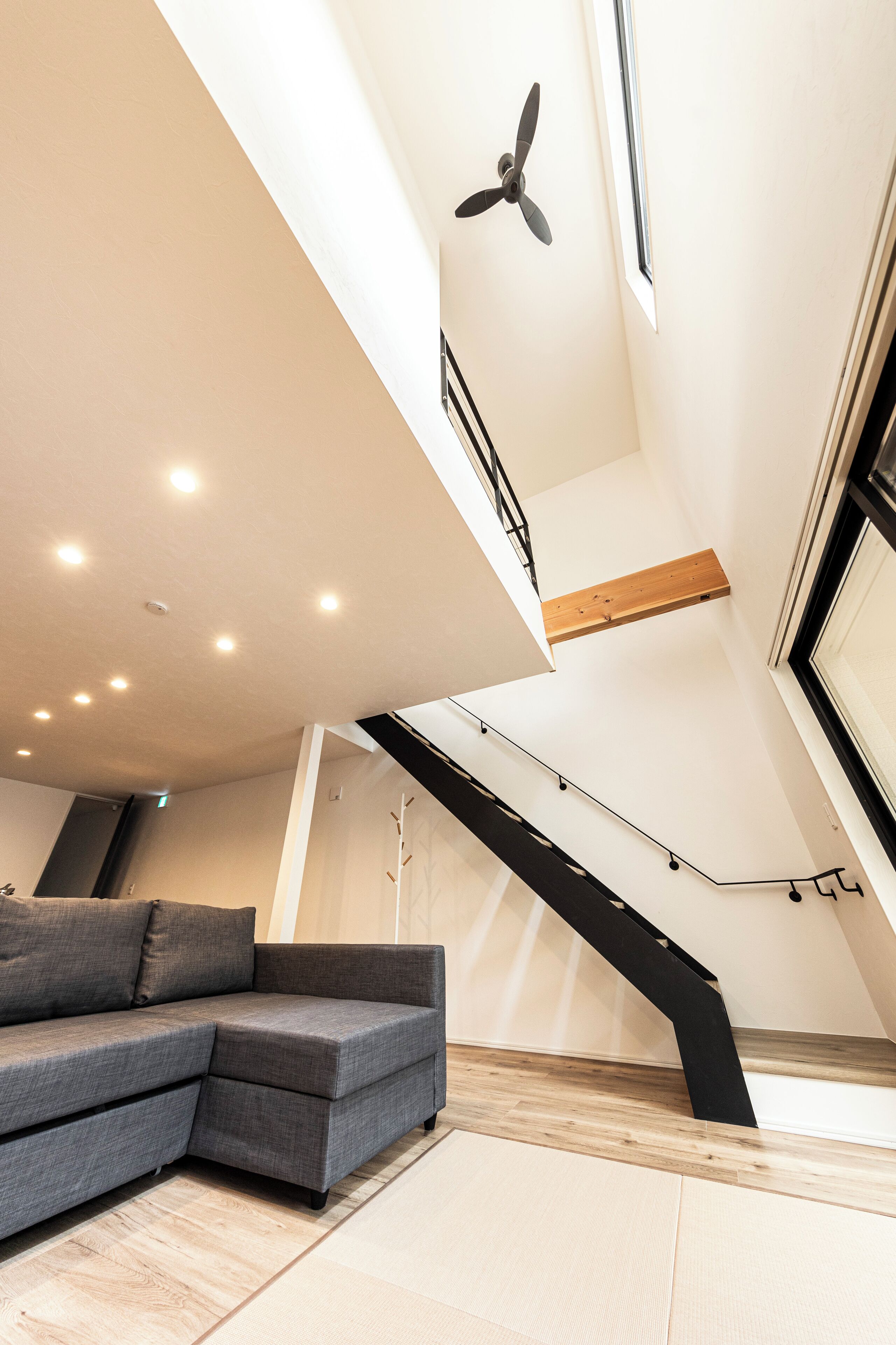 A modern living room with a grey sectional sofa, a wooden beam ceiling, and a black spiral staircase.