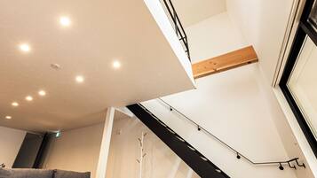 A modern living room with a grey sectional sofa, a wooden beam ceiling, and a black spiral staircase.