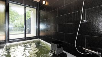 Un baño moderno con una pared de azulejos negros, una puerta de cristal que da al exterior y una zona de ducha.