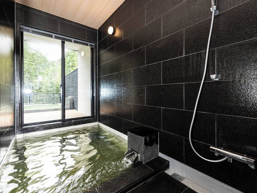 Un baño moderno con una pared de azulejos negros, una puerta de cristal que da al exterior y una zona de ducha.