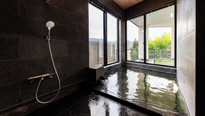 A modern bathroom with a glass-enclosed hot tub, large windows, and a shower area.