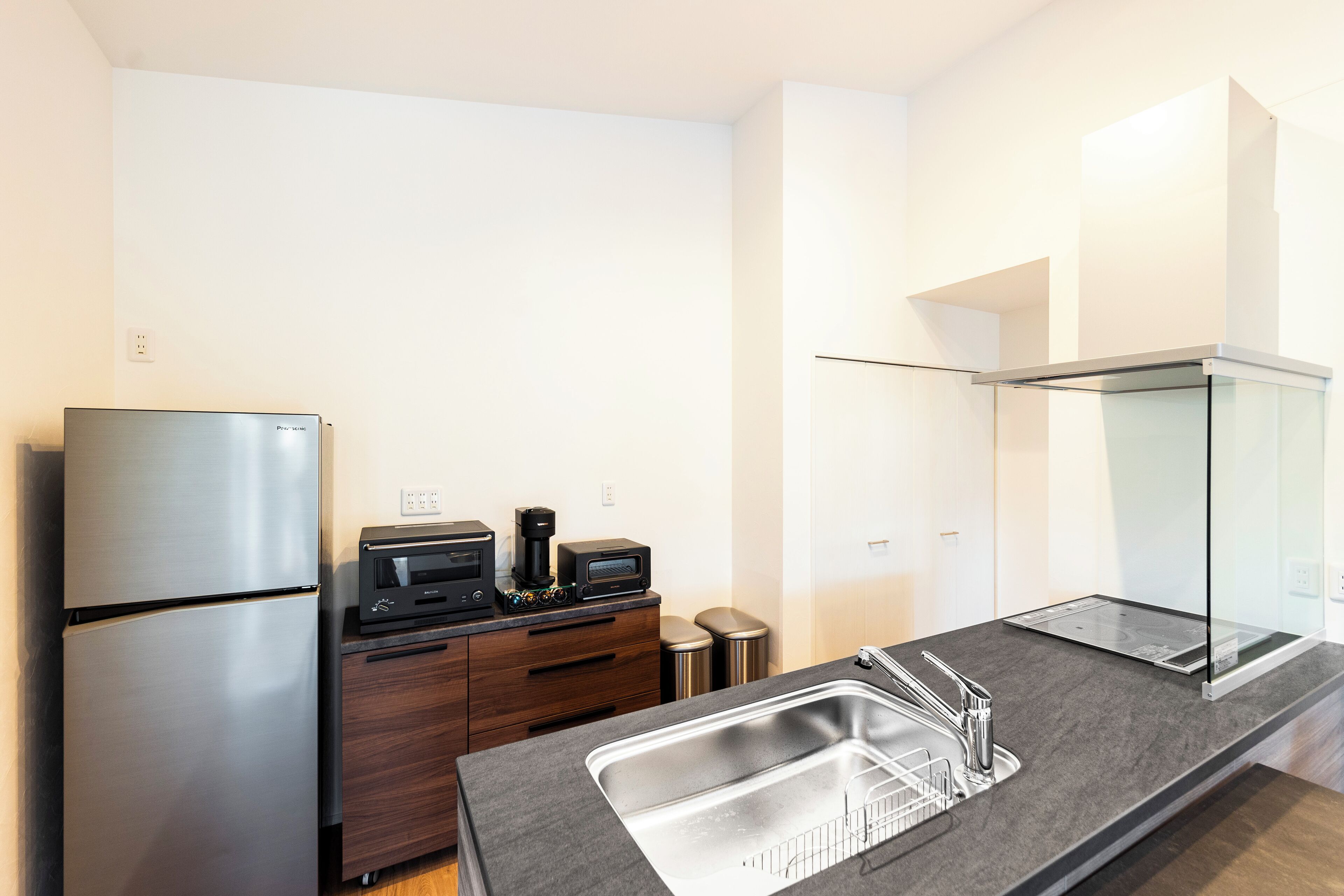 A modern kitchen with a stainless steel refrigerator, a microwave, a coffee maker, and a sink with a glass backsplash.