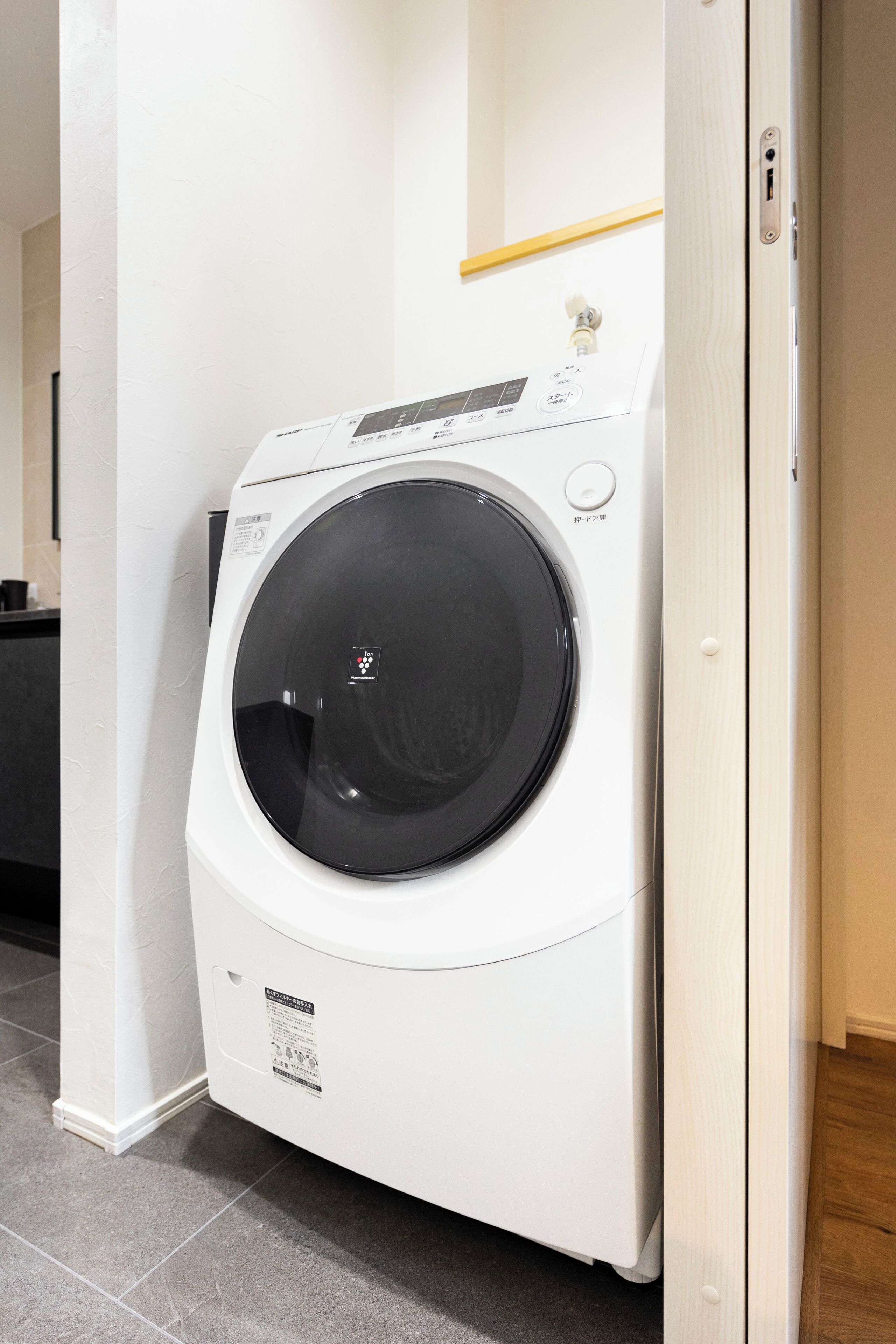 A front-loading washing machine in a room with tiled flooring and a wooden door.