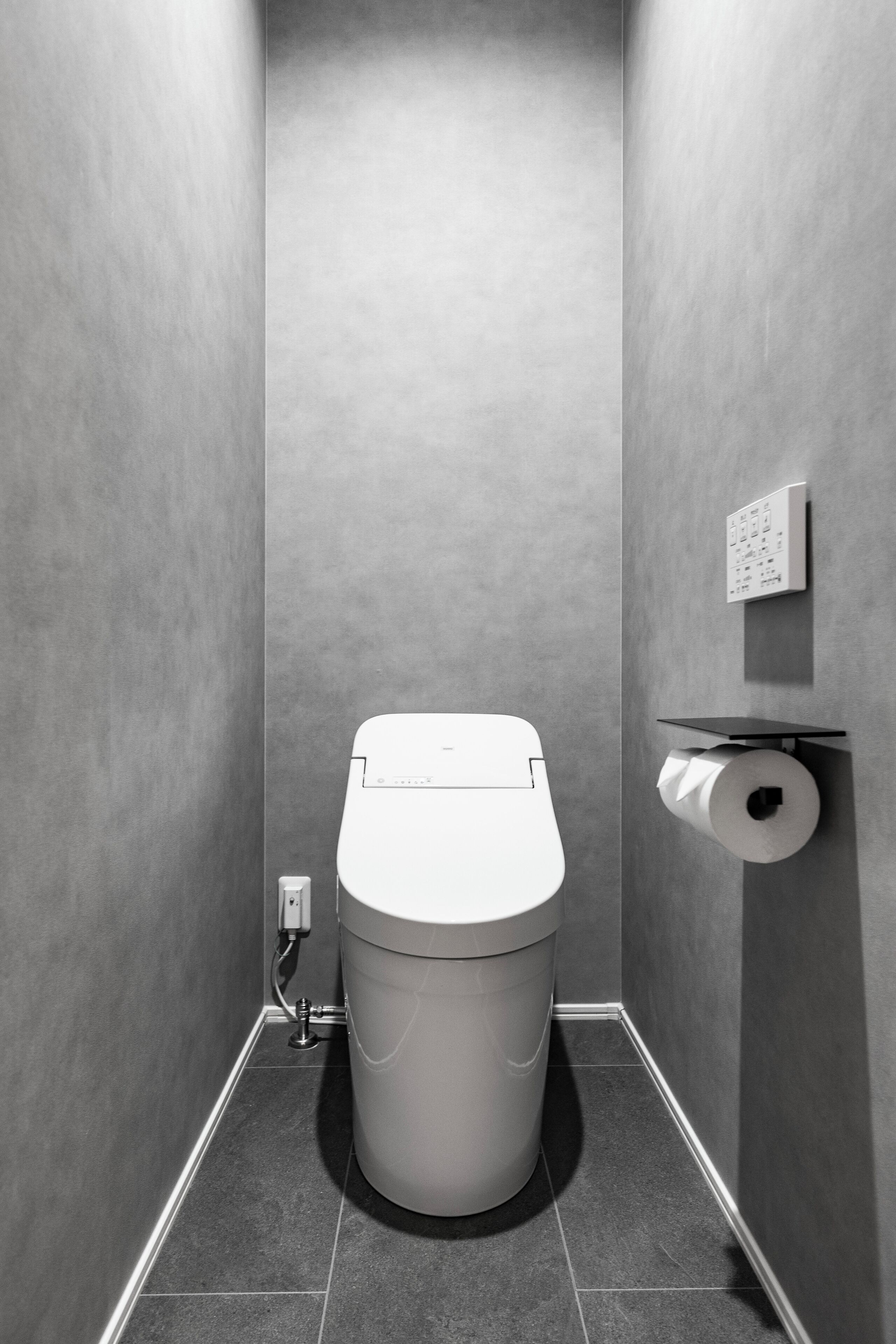 Een moderne badkamer met een toilet, een papieren handdoekdispenser en een in de muur gemonteerde spoelknop.