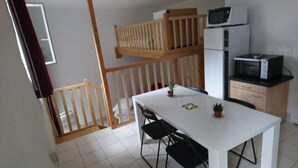 Una cocina compacta con una mesa blanca, dos sillas, un microondas y un refrigerador.