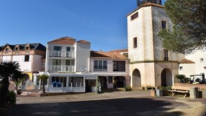 Ein Gebäude mit einem Turm, einem überdachten Bereich mit Sitzgelegenheiten und einer Straße davor.