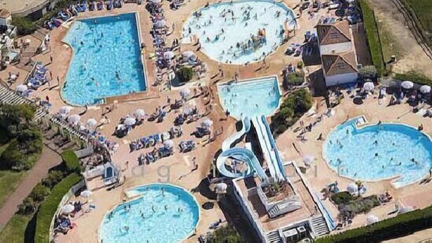 Eine Luftaufnahme eines Resorts mit mehreren Schwimmbecken, Liegebereichen und einer Wasserrutsche.