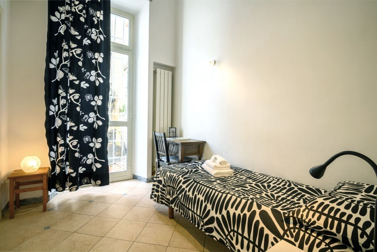 A bedroom with a bed, a desk, a chair, a lamp, and a window with curtains.