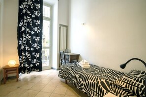 Un dormitorio con una cama, un escritorio, una silla, una lámpara y una ventana con cortinas.