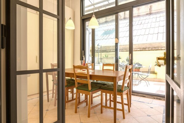 A dining area with a table and chairs, large windows, and a view of the outside.