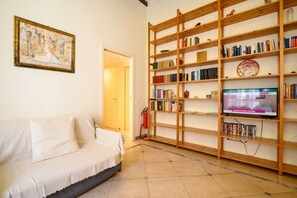 Ein Zimmer mit einem weißen Sofa, einem Bücherregal, einem Gemälde und einem Fernseher.