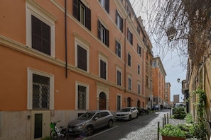 A narrow cobblestone street lined with multi-story buildings, parked cars, and a bicycle. - Quattro Cantoni Apartment Monti (Roma)