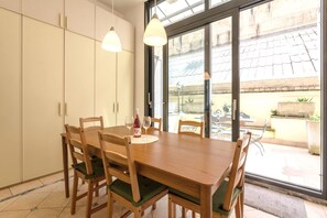 A dining area with a wooden table and chairs, a bottle of wine, and a glass. There are two pendant lights above the table.