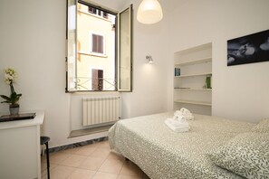 Ein Schlafzimmer mit Bett, Heizkörper, Fenster, einem Regal mit Büchern und einer Topfpflanze.