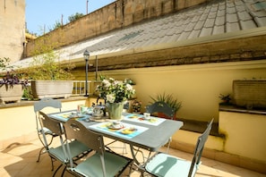 An outdoor patio with a table set for two, surrounded by chairs, a potted plant, and a street view. - Quattro Cantoni Apartment Monti (Roma)