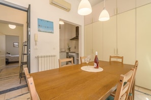 A dining area with a wooden table, chairs, and a bottle of red wine. There is a kitchen in the background with a stove and cabinets. - Quattro Cantoni Apartment Monti (Roma)