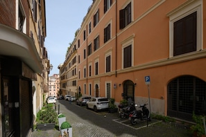 A narrow street lined with multi-story buildings, parked cars, and a motorcycle.