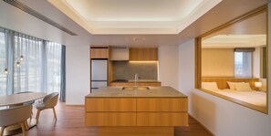 A modern hotel room with a wooden dining table, chairs, a kitchen area with a built-in stove, and a large bed with a nightstand. - HOTEL LA VIGNE HAKUBA by Onko Chishin (Hakuba)
