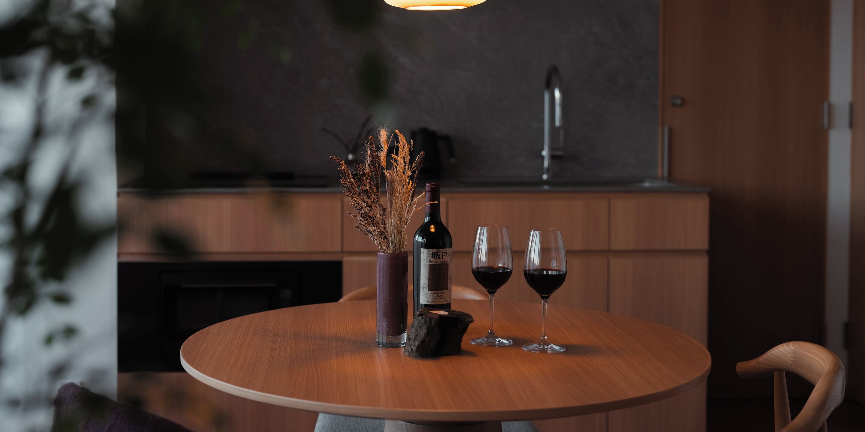 A round wooden table with a bottle of wine and two wine glasses on it.