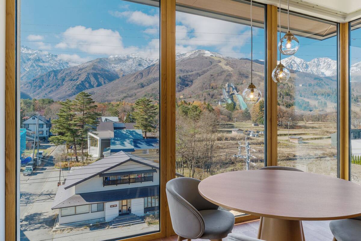 A room with a large window offering a mountain view, a round table, and two chairs.