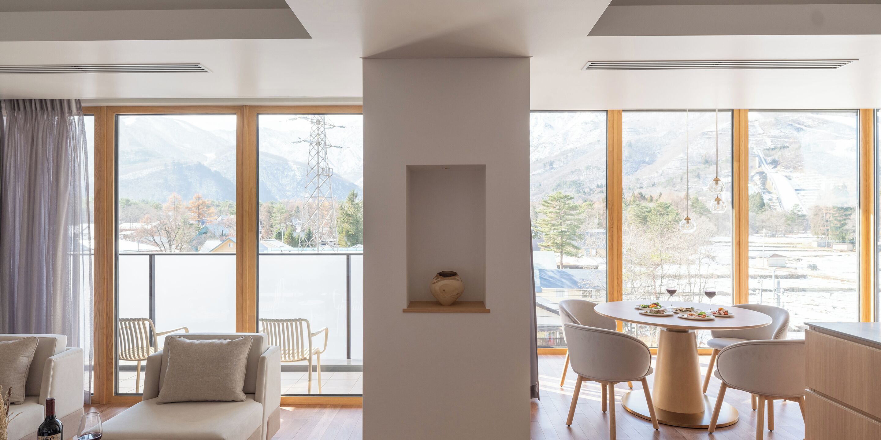 A modern living room with a sofa, chairs, a dining table, and a view of mountains through large windows.
