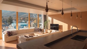 A modern kitchen with a large island, wooden cabinets, and a built-in oven. There is a seating area with a sofa and a dining table. - HOTEL LA VIGNE HAKUBA by Onko Chishin (Hakuba)