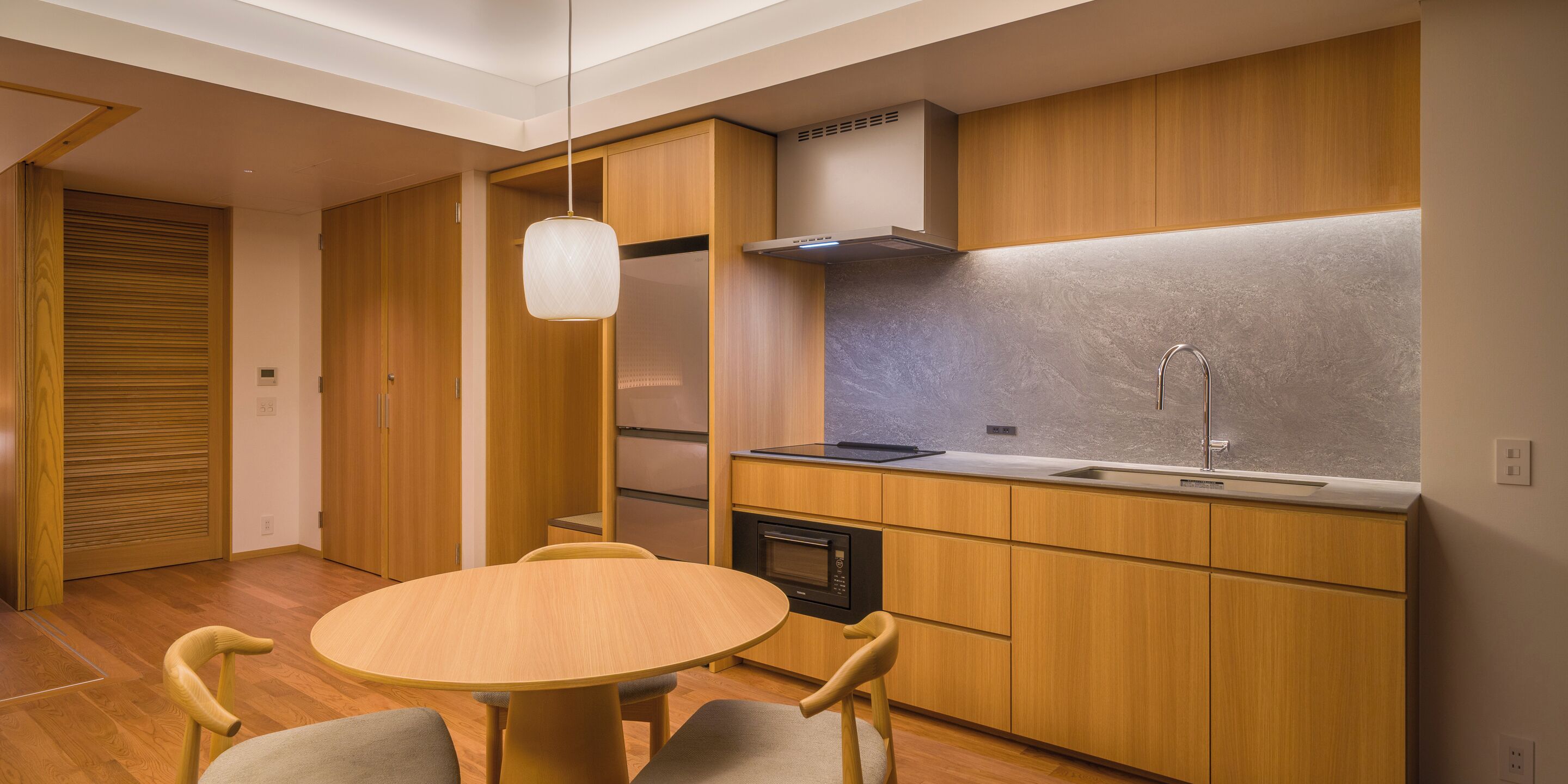 A modern kitchen with wooden cabinets, a built-in oven, and a round dining table with chairs.