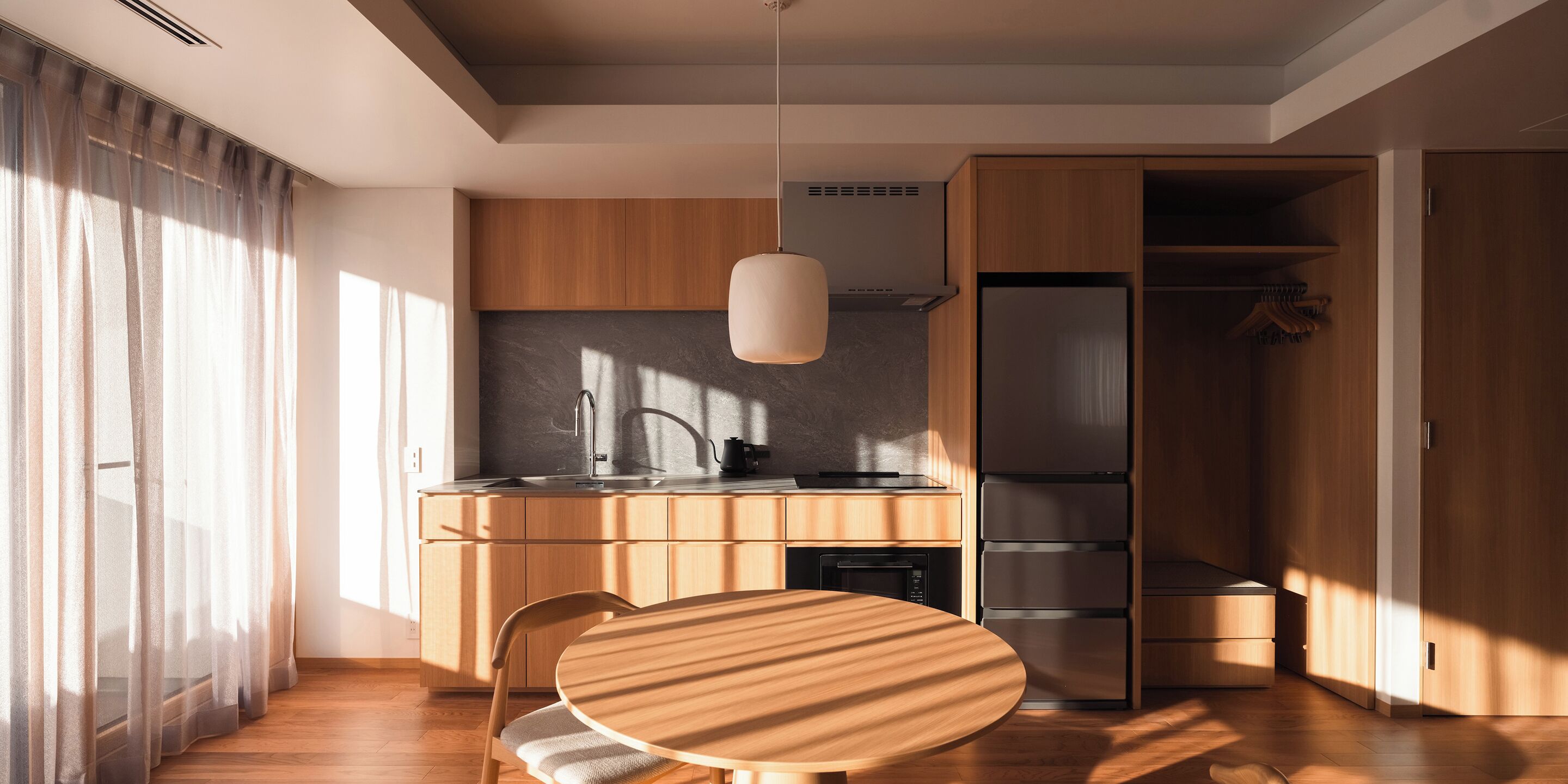 Una cocina moderna con armarios de madera, un refrigerador de acero inoxidable y una mesa redonda de madera con una silla.